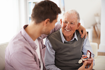 Image showing Father, adult son and medal for present support and congratulations with celebration and bonding at home. Men in living room, family time with reward or award as gift for happiness and gratitude