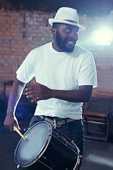 Image showing Smiling, black man and playing drum or music for event, concert with percussion and entertainment. Festival, performance and beats on rhythm for band of a creative on stage with white shirt and hat