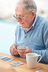 Image showing Elderly man, coffee and playing cards on table for poker, relax and happy in retirement. Senior person, grandfather and beverage with thinking, hobby and fun strategy on patio in home drinking tea