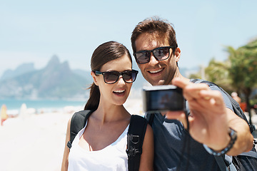 Image showing Couple, beach and camera for selfie on holiday with smile, sunglasses and outdoor for memory in summer. People, man and woman with photography by ocean for journey, vacation and sunshine in Italy