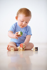 Image showing Baby boy, wooden blocks and playing with toys in early childhood development on a gray studio background. Little toddler or child on floor with shape or cube in building, learning or cognitive skills