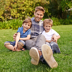 Image showing Smile, nature and portrait of children with father relaxing on grass in outdoor park or garden. Happy, family and excited cute boy kids sitting on lawn with young dad for bonding in field together.