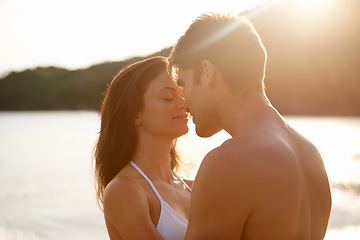 Image showing Love, kiss and couple on island for date on romantic anniversary vacation, adventure or holiday. Smile, bonding and young man and woman embracing with care by ocean at sunset on weekend trip together