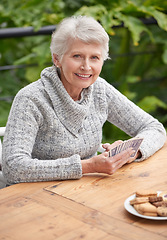 Image showing Elderly woman, cookies and portrait with cards at table for relaxation, old age and retirement. Senior person or grandmother and smiling with wrinkles for poker game, gamble and hobby for leisure