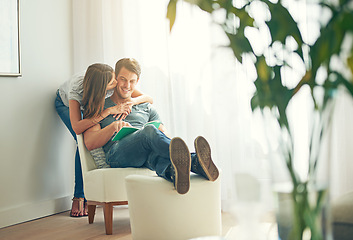 Image showing Couple, embrace and read in house, love and chair to relax and hugging for learning and kiss. Man, woman and romance while happy, smile and book for entertainment and together in living room at home