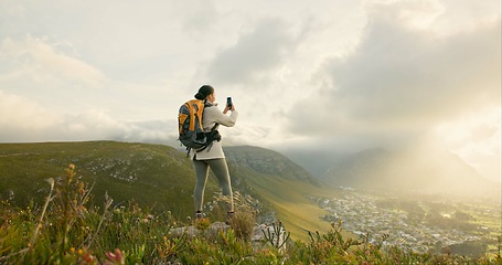 Image showing Woman, trekking and video recording on mountains in adventure, wellness and health with nature and cityscape. Person with backpack and hiking photography on green hill, travel or eco friendly journey