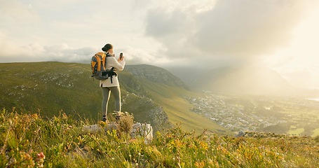 Image showing Woman, hiking and video recording on mountains in adventure, wellness and health with nature and cityscape. Person with backpack and trekking photography on green hill, travel or eco friendly journey