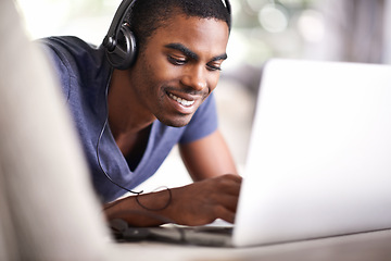 Image showing Man, face and music with laptop in home for internet streaming, podcast and online research with smile. Student, black person and technology with headphones for relax, studying and learning on couch