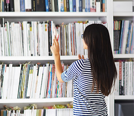 Image showing Student, woman and back by bookshelf with search, studying and development at university for knowledge. Person, girl and research in library with books, check and inspection for learning at college