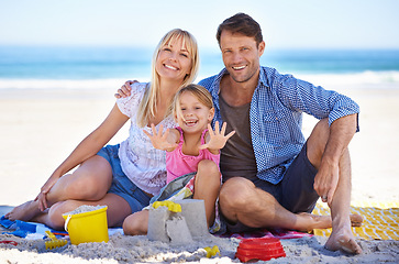 Image showing Parents, girl and sandcastle in portrait at beach, blanket and excited with hug for holiday in summer. Father, mother and daughter with picnic by ocean for vacation in nature with love in sunshine