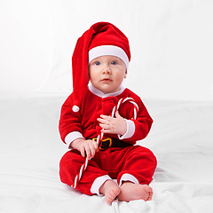 Image showing Baby, portrait and cute with santa outfit for first Christmas holiday, candy cane and white background. Boy toddler, xmas and costume for festive season or celebration, innocent and adorable with hat