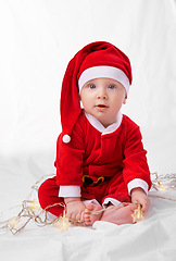 Image showing Baby, portrait and cute with santa costume for first Christmas holiday, star lights and white background. Boy toddler, xmas and outfit for festive season or celebration, innocent and adorable in hat.