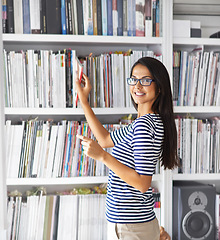 Image showing Woman, portrait and happy by bookshelf in home with books for reading, learning and knowledge in living room. Person, face and smile by library in house with magazine, journal and study collection