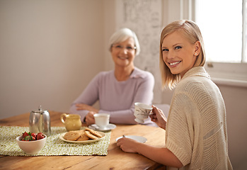 Image showing Portrait, happy woman and elderly mother drinking tea at breakfast, bonding and smile in house. Face, senior mom and daughter with coffee cup at table, food and family eating cookies at home together