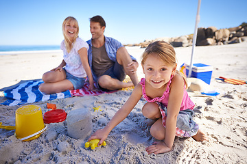 Image showing Parents, girl and sandcastle in portrait by sea, blanket and excited with building for holiday in summer. Father, mother and daughter with family picnic by ocean for vacation with smile in sunshine