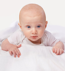 Image showing Baby, blue eyes and shock with laying on bed for curiosity, surprise and reaction in bedroom at house. Adorable, child and cute infant with vest in home to observe, relax wonder for knowledge