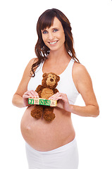 Image showing Pregnancy, woman and smile with blocks in studio for name reveal, announcement or news of daughter. Mother, belly and teddy bear on abdomen with growth, wellness or future plan on white background