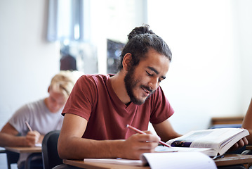 Image showing College, student and man with smile for learning with textbook, scholarship and studying for education. Male person, happy and reading for information with research on table or desk of classroom