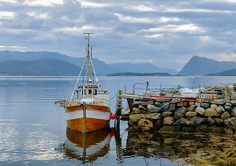 Image showing Fishing boat moored at a rustic stone pier in serene coastal wat