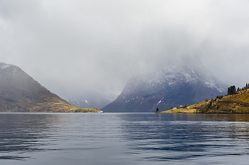 Image showing Misty fjord surrounded by snow-capped mountains during a calm wi