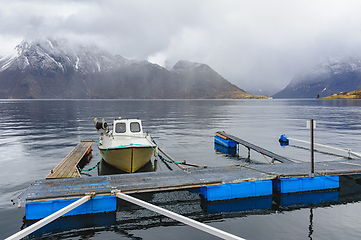 Image showing Small boat moored at a wooden dock on a calm mountain fjord duri