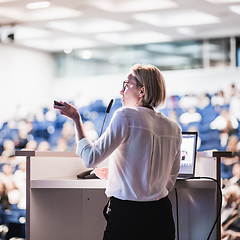Image showing Female speaker giving a talk on corporate business conference. Unrecognizable people in audience at conference hall. Business and Entrepreneurship event.