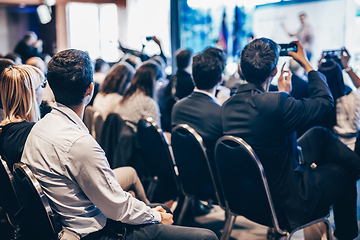 Image showing Speaker giving a talk in conference hall at business event. Rear view of unrecognizable people in audience at the conference hall. Business and entrepreneurship concept.