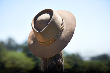 Image showing Cowboy hat, outdoor and wood post for protection from sun with fashion at ranch, countryside and nature. Vintage cap, headwear and shade from sunshine with farming, agriculture and summer in Texas