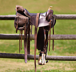 Image showing Saddle, horse and farm on ranch fence, riding and equestrian sports in country side. Western, cowboys and field in Texas, stirrup and leather seat or equipment for outdoors exercise in paddock
