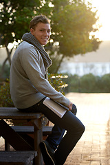 Image showing Student, man and outdoor on campus with book in smile, study and prepare for exam with revision notes. Portrait, college and academic for assignment with textbook for education and learning.