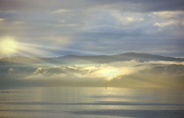 Image showing Sea, sunset and cloud on mountains in morning, reflection and island with landscape in nature. Blue sky, clouds or sunlight on water on beach, calm or sunrays on sustainable environment or seascape