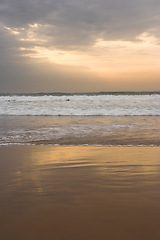 Image showing Beach, sunset and ocean on sand with clouds in sky on vacation, holiday on tropical island with rain. Sea, landscape and travel outdoor with calm waves, water and horizon in nature or environment