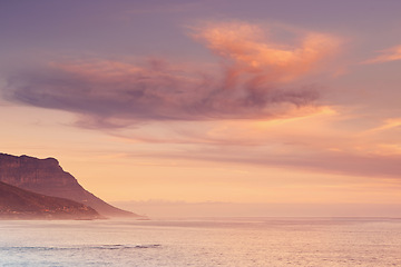 Image showing Ocean, sunset and calm water by mountain and tourism destination for summer vacation in nature. Blue sky, clouds and neon color on cape town beach, peace and outdoor travel with sunshine in paradise