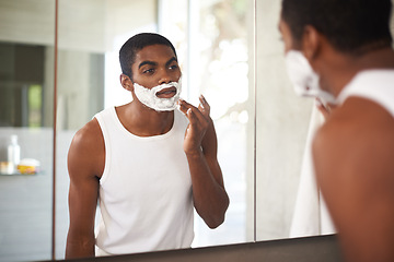 Image showing Black man, mirror and shaving cream on face in bathroom for grooming, skincare or morning routine. Reflection, beard and person apply foam for cleaning, health and hair removal for hygiene in home