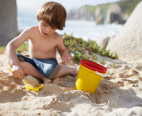 Image showing Sand castle, beach and child with bucket and toys on summer holiday, vacation and relax by ocean. Childhood, building or digging and young boy playing for adventure, fun and weekend by seaside