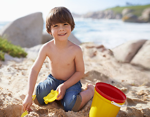 Image showing Sand castle, beach and portrait of child with bucket and toys on summer holiday, vacation and relax by ocean. Childhood, building sandcastle and young boy playing for adventure, fun or weekend by sea