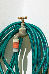 Image showing Tap, pipe and garden hose with attachment for water, pressure or environmental care at home. Closeup of faucet with plastic hosepipe rolled up on wall for liquid supply, service or outdoor gardening