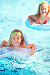 Image showing Swimming, inflatables and portrait of kids in pool, playing and summer at resort on vacation. Holiday, games and friends relax in water with toys for fun, activity or children with safety gear