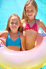 Image showing Girls, summer and pool with inflatable tube on vacation, swimwear and fun in sunlight for holiday. Happy, kids ad entertainment with smile and toy, children in water for swimming together outdoors