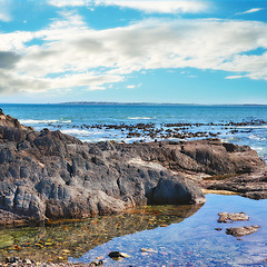 Image showing Rocks, sea and landscape with nature, blue sky and clouds with coastline and outdoor travel destination. Surf, Earth and water with ocean view, natural background and beach location in Cape Town