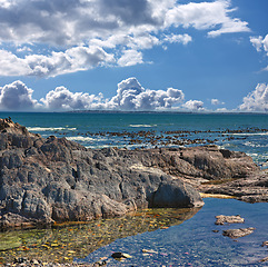 Image showing Rocks, ocean and landscape with nature, blue sky and clouds with coastline and outdoor travel destination. Surf, Earth and water with seascape, natural background and beach location in Cape Town