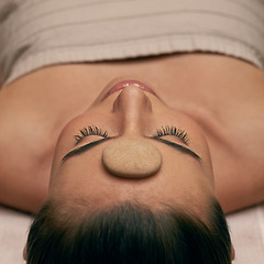 Image showing Massage, spa and stone on head of woman on table to relax with stress relief or luxury treatment. Calm, wellness and zen with young beauty customer on table for balance, inner peace or mindfulness