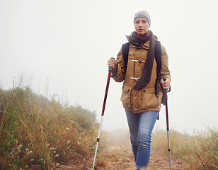 Image showing Woman, hiking and outdoor with trekking sticks, winter and support for fog trail in mountain. Athlete, backpack and sport gear for safety in wet environment, slippery and walking in cold for fitness