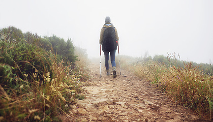 Image showing Person, hiking and back in field with trekking sticks, adventure and support for fog trail in mountain. Athlete, backpack and sport gear for safety in wet environment, healthy and walking for fitness