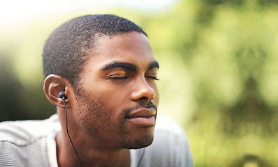 Image showing Face, music and relax with black man in garden or park outdoor for summer, peace and quiet. Nature, radio and wellness with calm young person streaming audio or sound on earphones in backyard