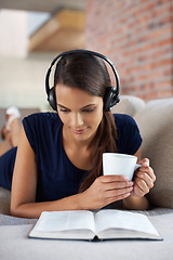 Image showing Music, book and woman relax with coffee in home on holiday or vacation and headphones streaming audio. Girl, reading and listening to sound on sofa in apartment on weekend with green tea or drink