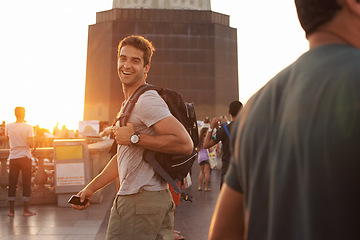Image showing Portrait, smile and man with backpack sunset, tourist and travel abroad for adventure or vacation. Happy person, laughing and holiday journey in city with casual outfit, smartphone and joyful face