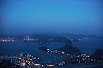 Image showing Aerial, night and city skyline by ocean, mountains and landscape view of urban buildings with lights. Drone, cityscape or coastline in rio brazil for holiday, tourism and travel destination by sea