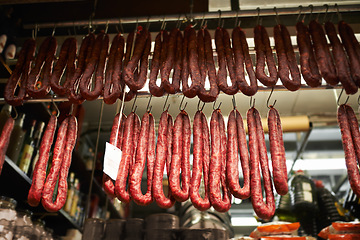 Image showing Hooks, butchery and dry sausage in shop for traditional food, groceries or products in Germany. Supermarket, meat and fermented or smoked salami hanging in row for production in grocery store.
