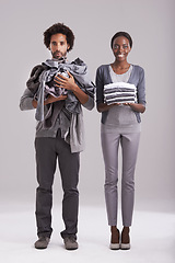 Image showing Portrait, studio and people with pile of clothes in hand for laundry day, wash or cleaning together. Woman, smile and washing folded with messy, man and annoyed for dirty wardrobe on gray background